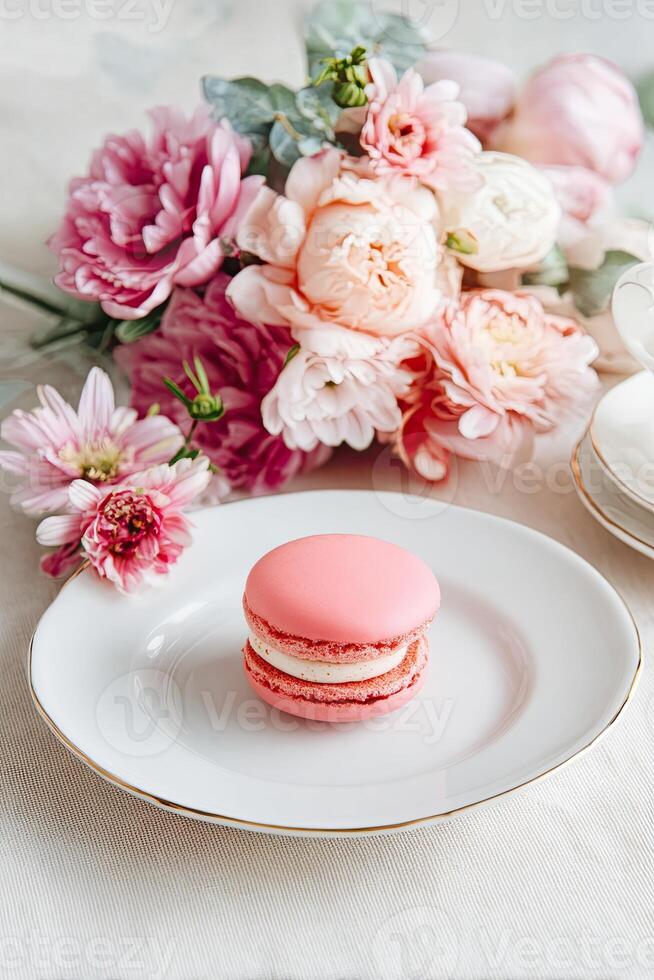 Pink macaron on elegant white plate with soft pastel flowers in romantic setting for dessert and beauty photo