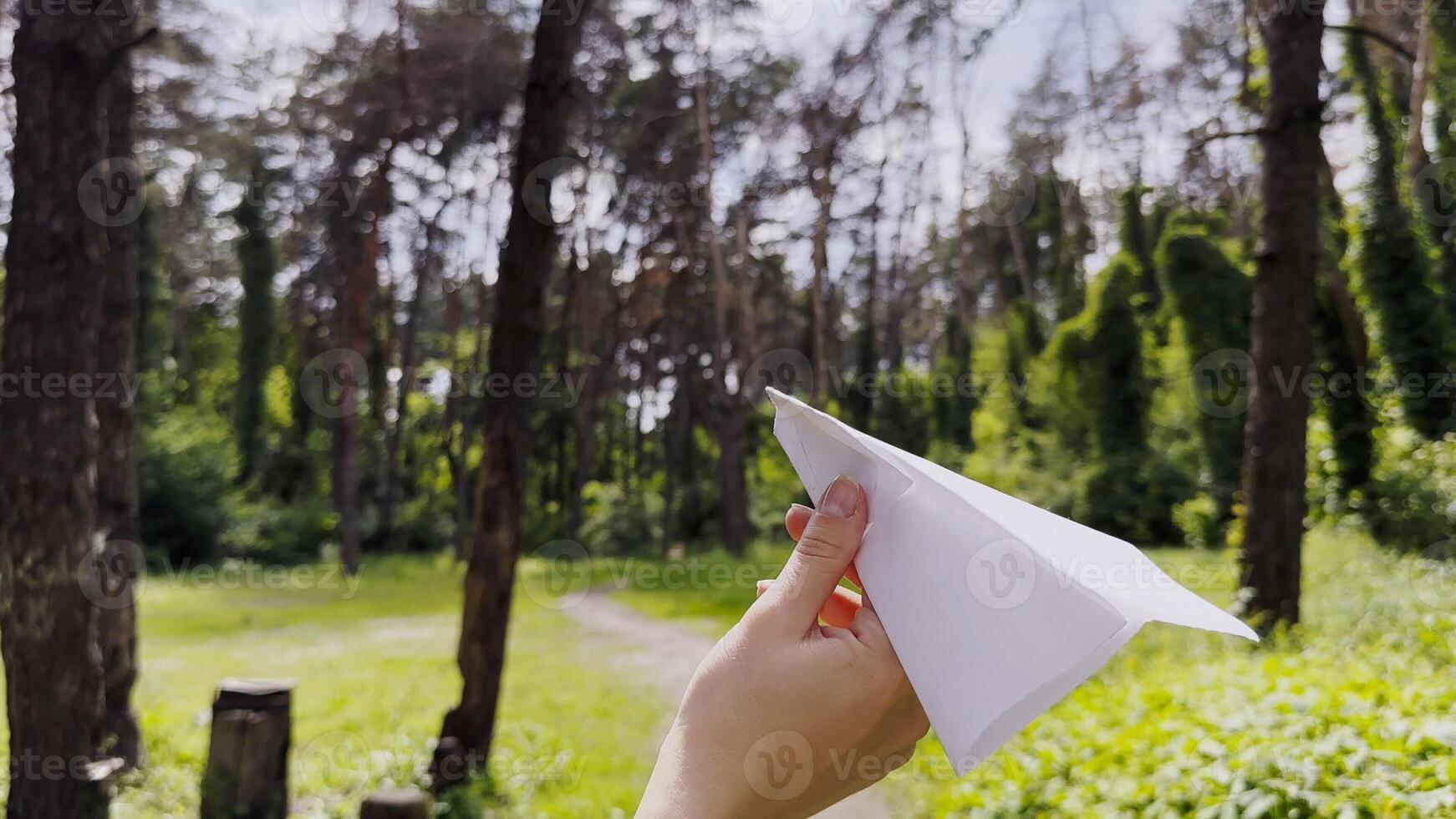 Female hand playing with paper airplane at summer forest. Girl walking with toy plane at woodland on sunny day. Young woman having fun at nature. Concept of leisure outdoor photo