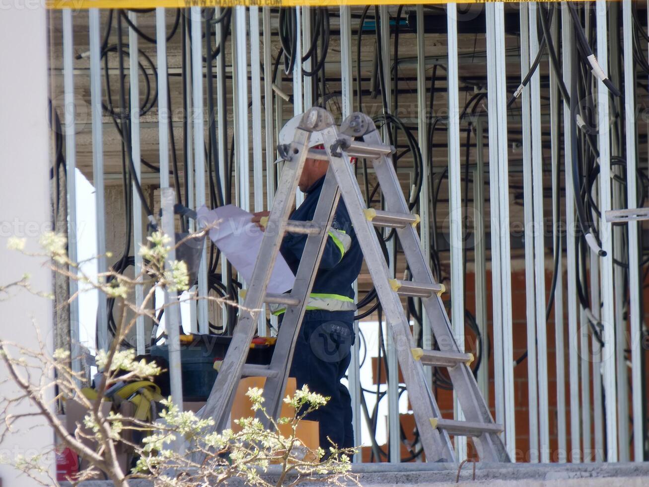 Worker on ladder reviewing plans during construction project at commercial site in bright daylight photo