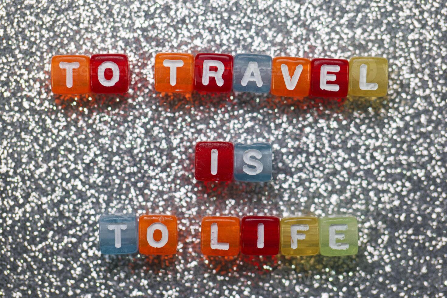 Travel as a vibrant expression of life captured in colorful letter blocks on a sparkling silver background photo