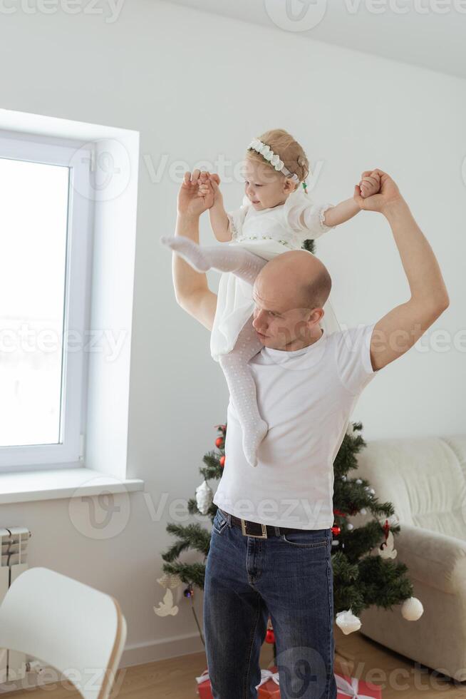 Baby child with hearing aid and cochlear implant having fun with father on christmas tree background. Deaf , diversity and health concept photo