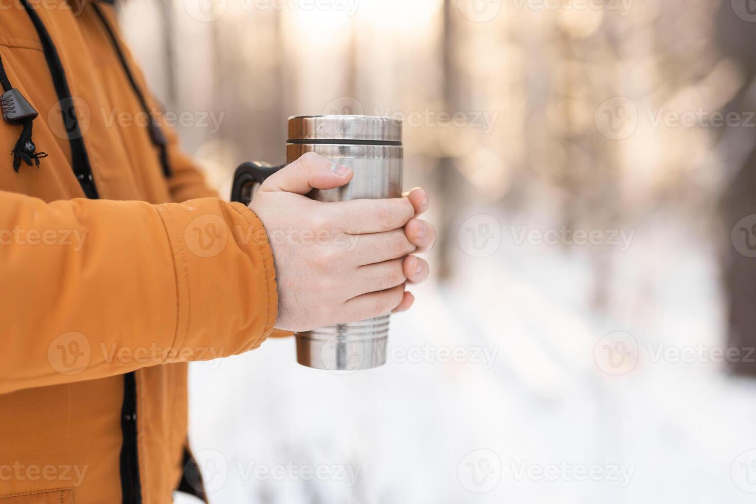 Man holding metal thermos in snowy forest during winter walk, copy space. Drink, mindfulness, and peaceful connection with nature through touch and seasonal routine photo