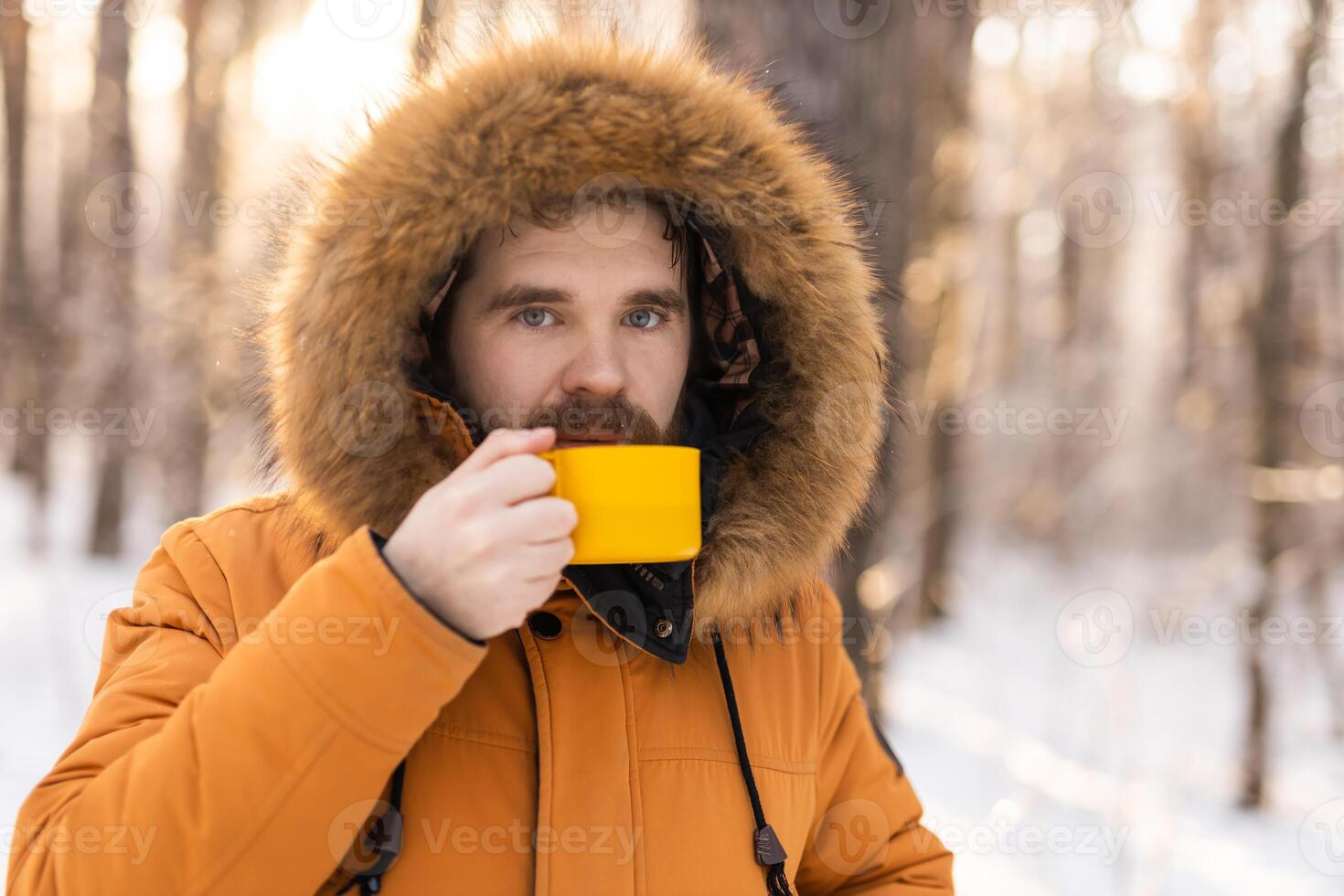 Man with yellow mug in snowy forest looking at camera. Mindfulness, warmth, and the human connection with nature during a quiet winter pause. Copy space photo
