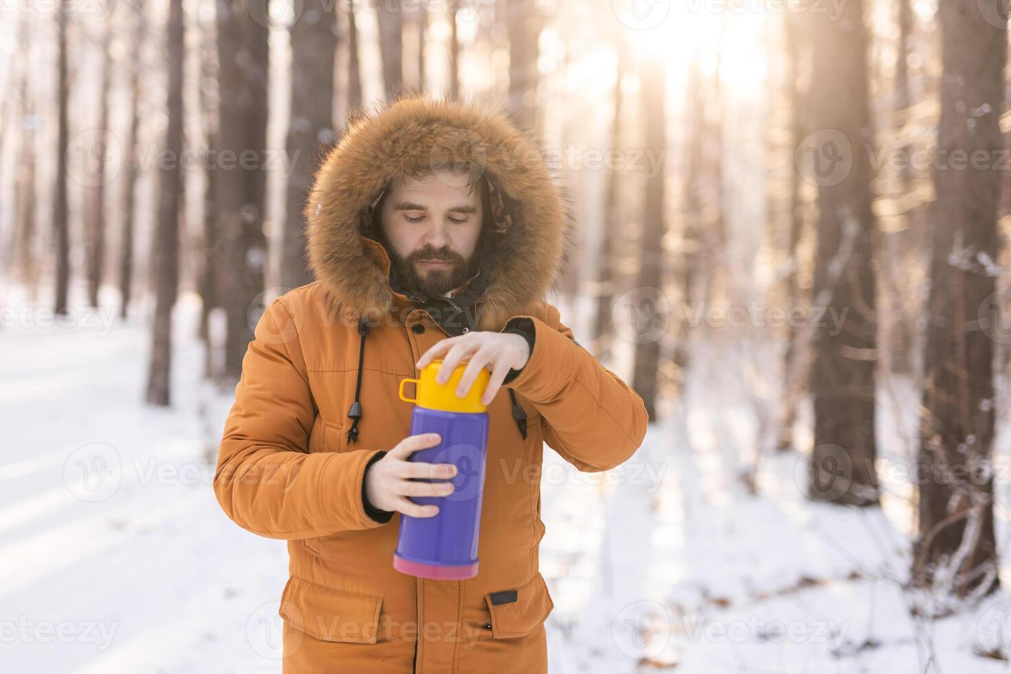 Close-up portrait handsome bearded millennial man in winter clothes and with thermos snow outdoor. Cold season and hot beverage in winter time, Copy space photo