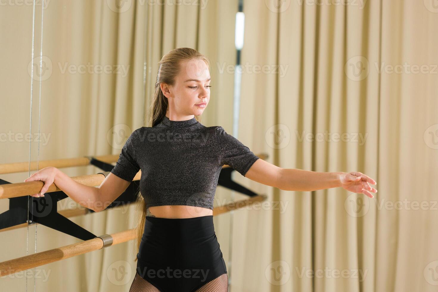 Young woman ballerina stretching and training at barre in dance studio - ballet and dancer concept photo