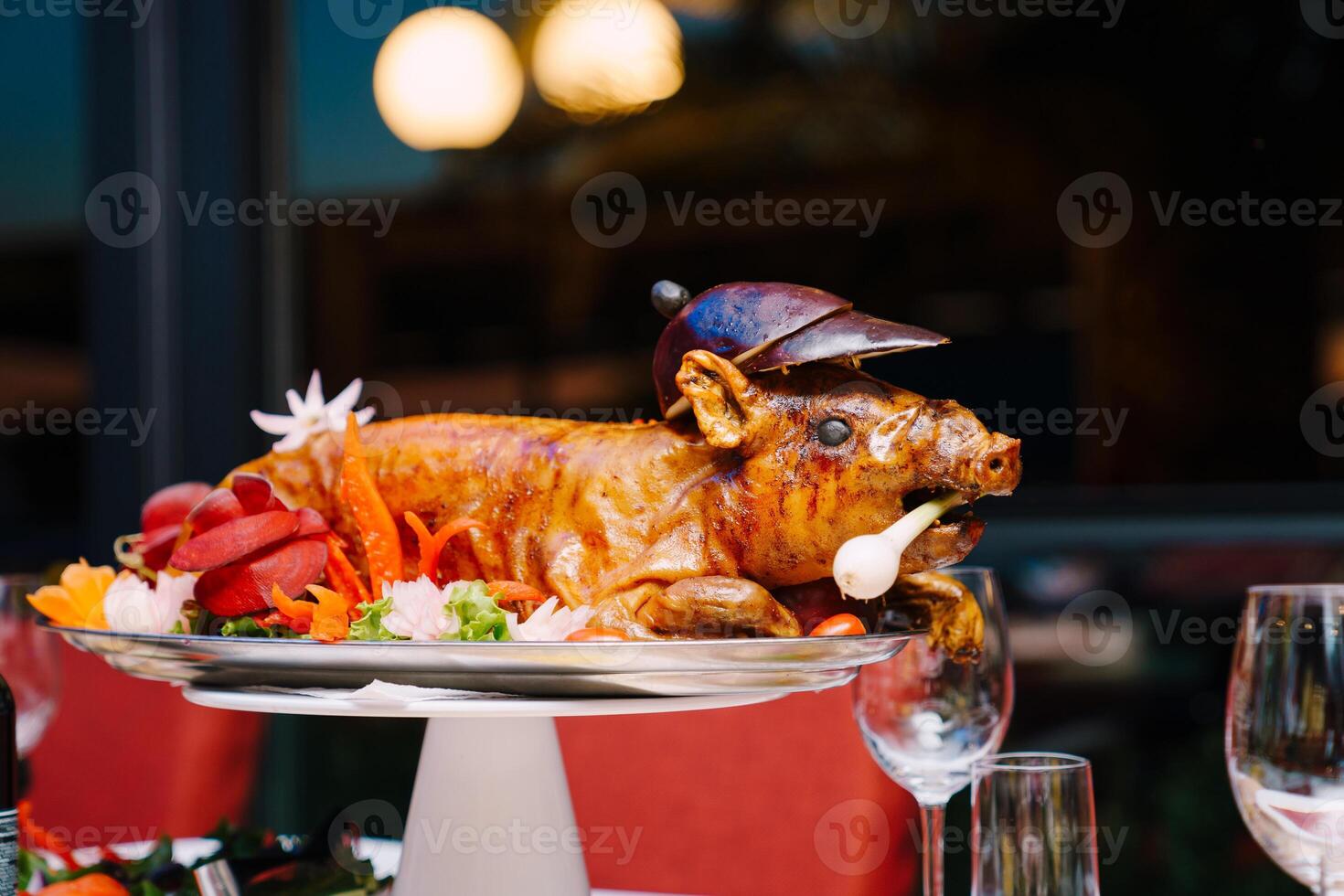 Roasted pig garnished with colorful vegetables lies on a platter on the table photo