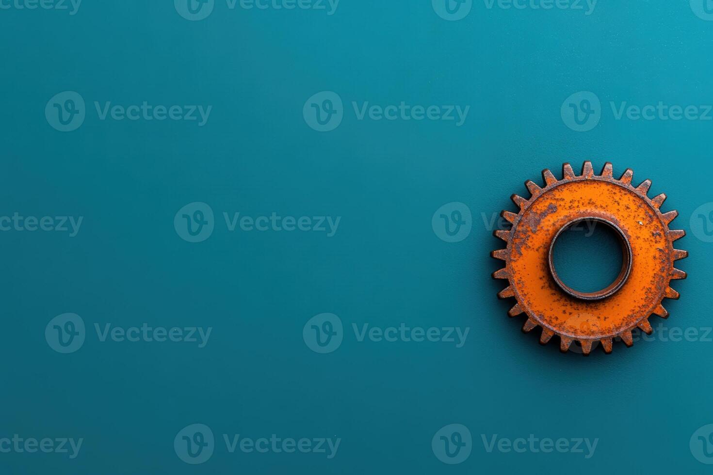 An old, rusted orange gear rests on a solid turquoise background, showcasing texture and color photo
