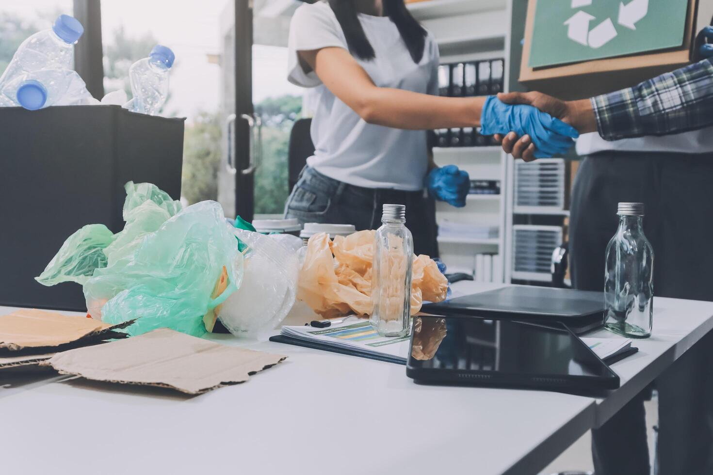 Two people shaking hands at a desk with trash and recycling photo