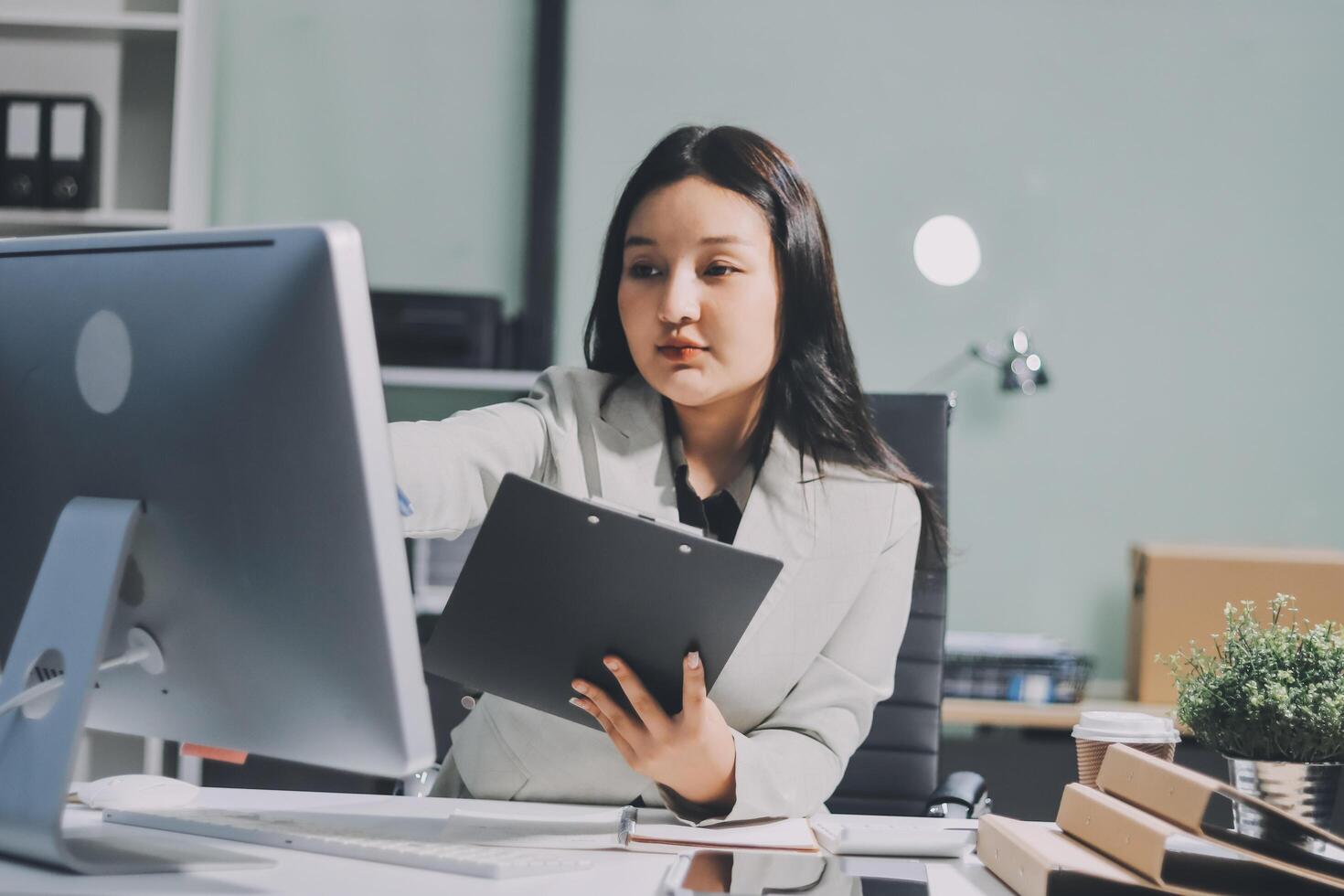 A woman is looking at a computer screen while sitting at a desk photo