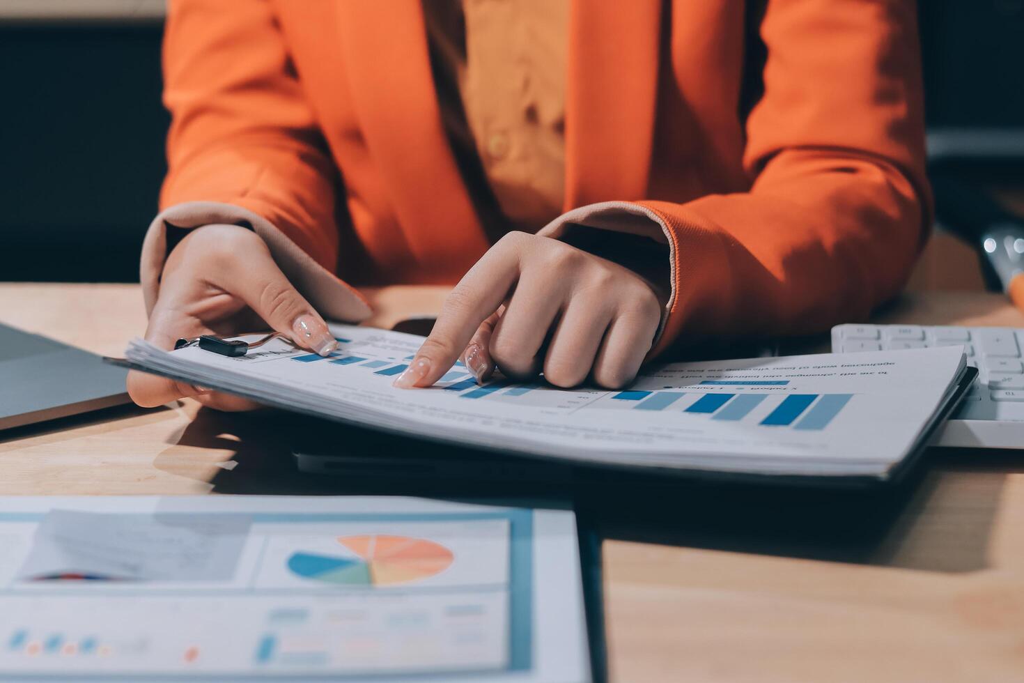 A woman in an orange jacket is looking at a document on a desk photo