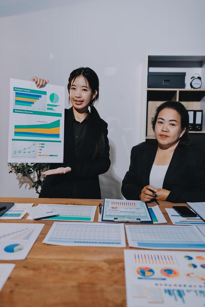 Two asian women in business attire holding up a chart photo