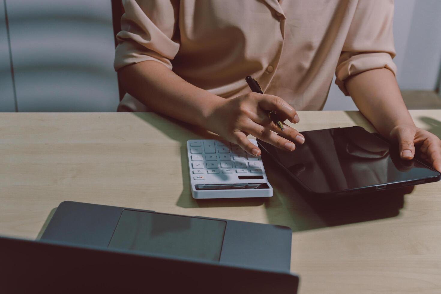 A woman is using a calculator and pen to write on a laptop photo