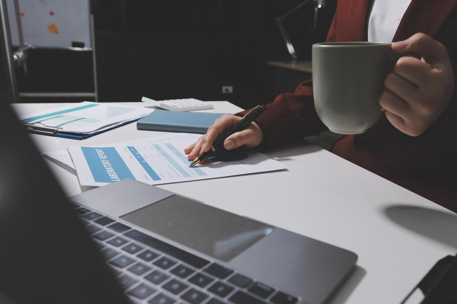 A person is working on paperwork while holding a coffee cup photo