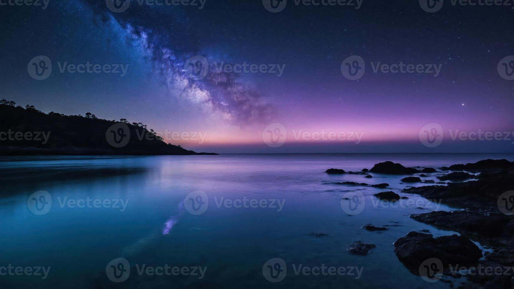 A serene nightscape featuring the Milky Way over calm waters and rocky shorelines. photo