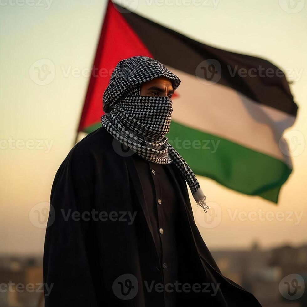 A man in a black jacket and a scarf stands in front of the palestinian flag photo