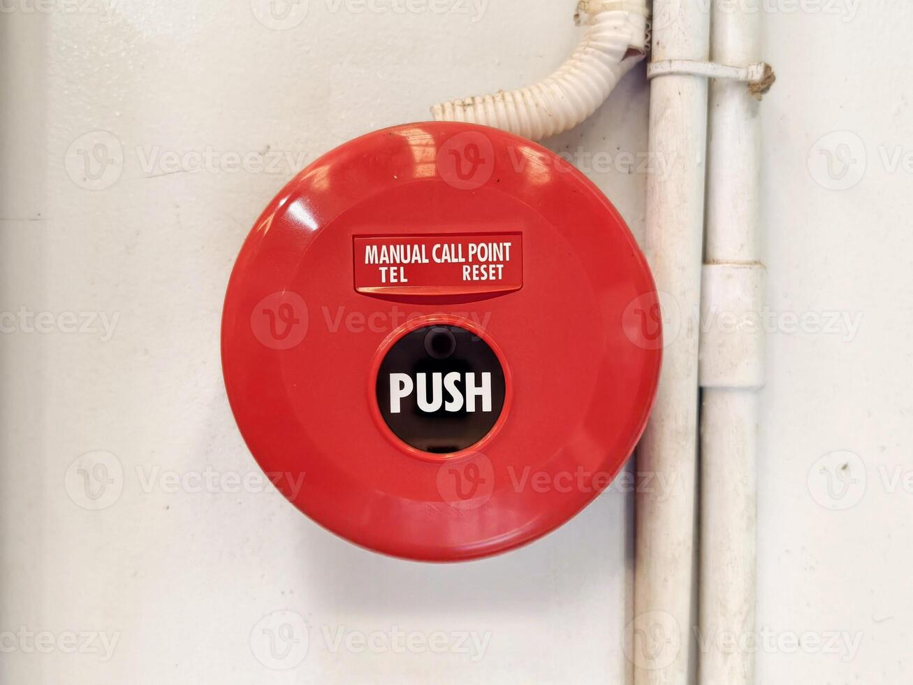 Red Manual Fire Alarm Call Point Mounted Beside Pipes on White Wall photo