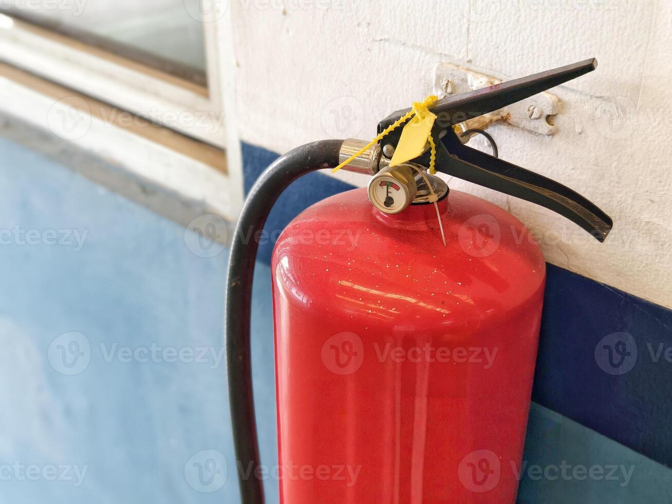 Close Up of Red Fire Extinguisher Mounted on Indoor Wall with Safety Seal photo
