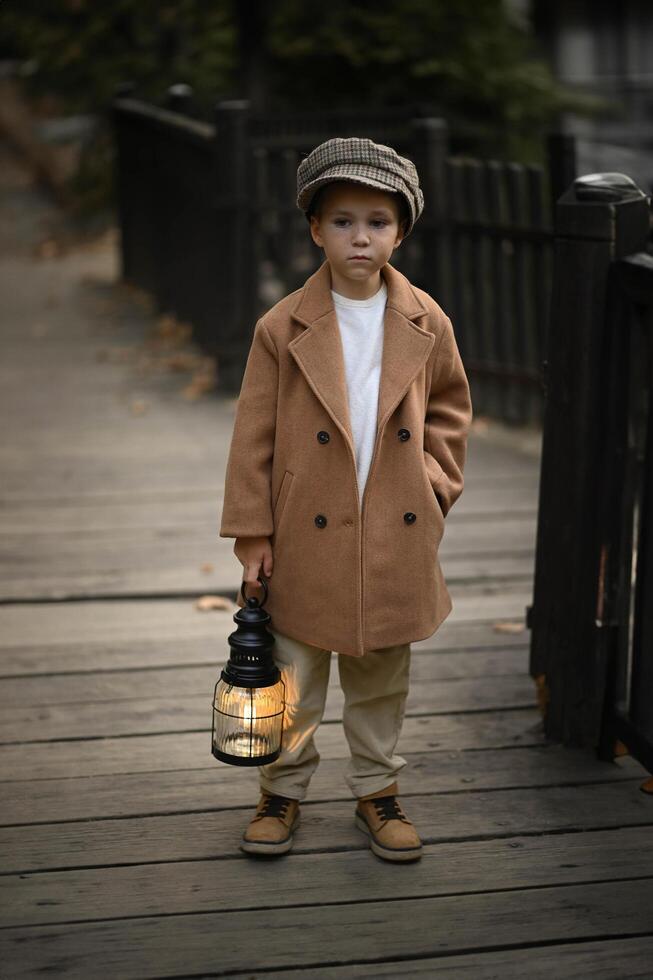 A young boy in vintage clothing and hat holds a lantern, standing quietly as the evening light fades. photo