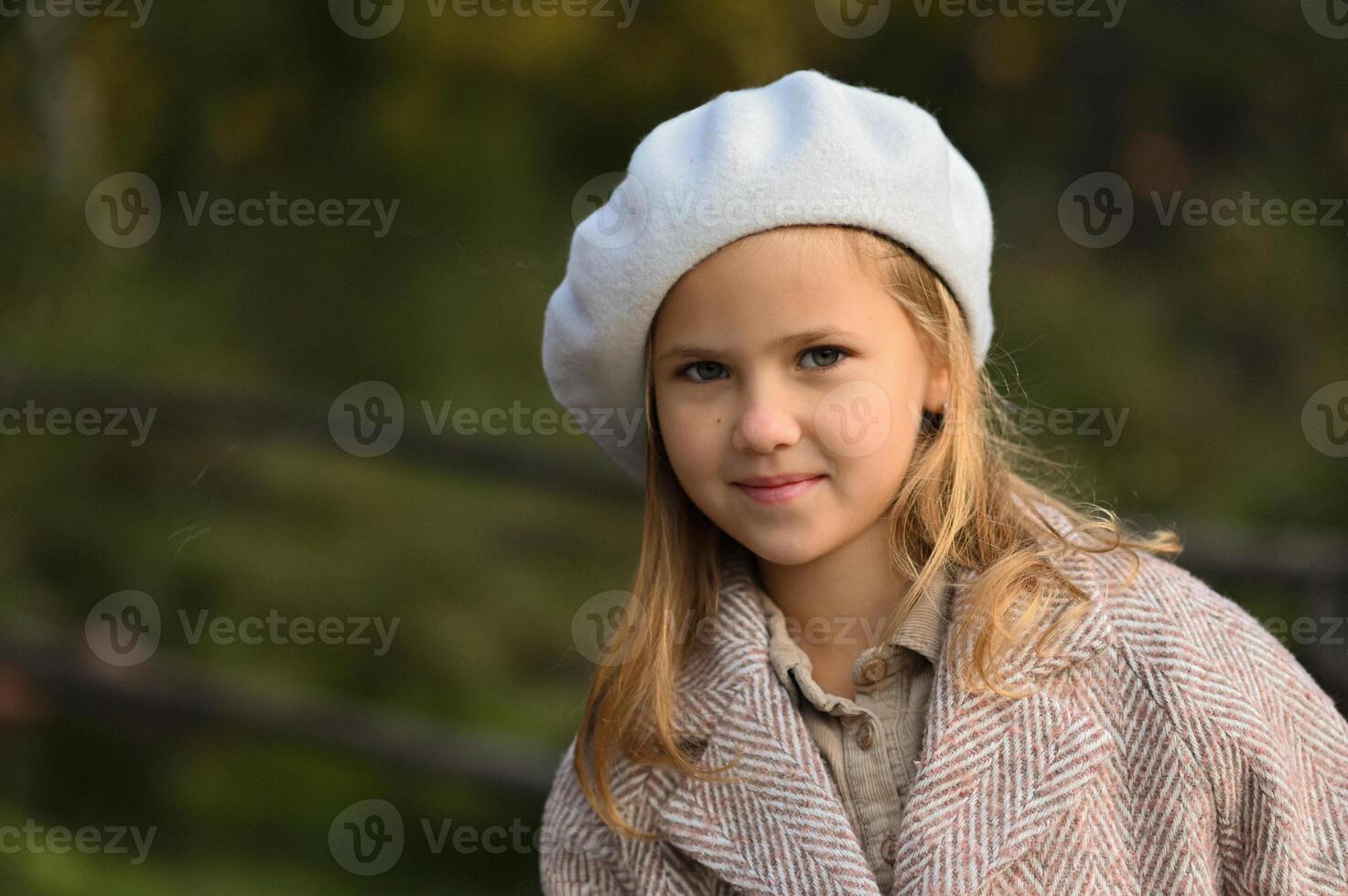 A young girl wearing a soft pink coat and a white beret gazes gently at the camera, her expression calm and thoughtful. photo