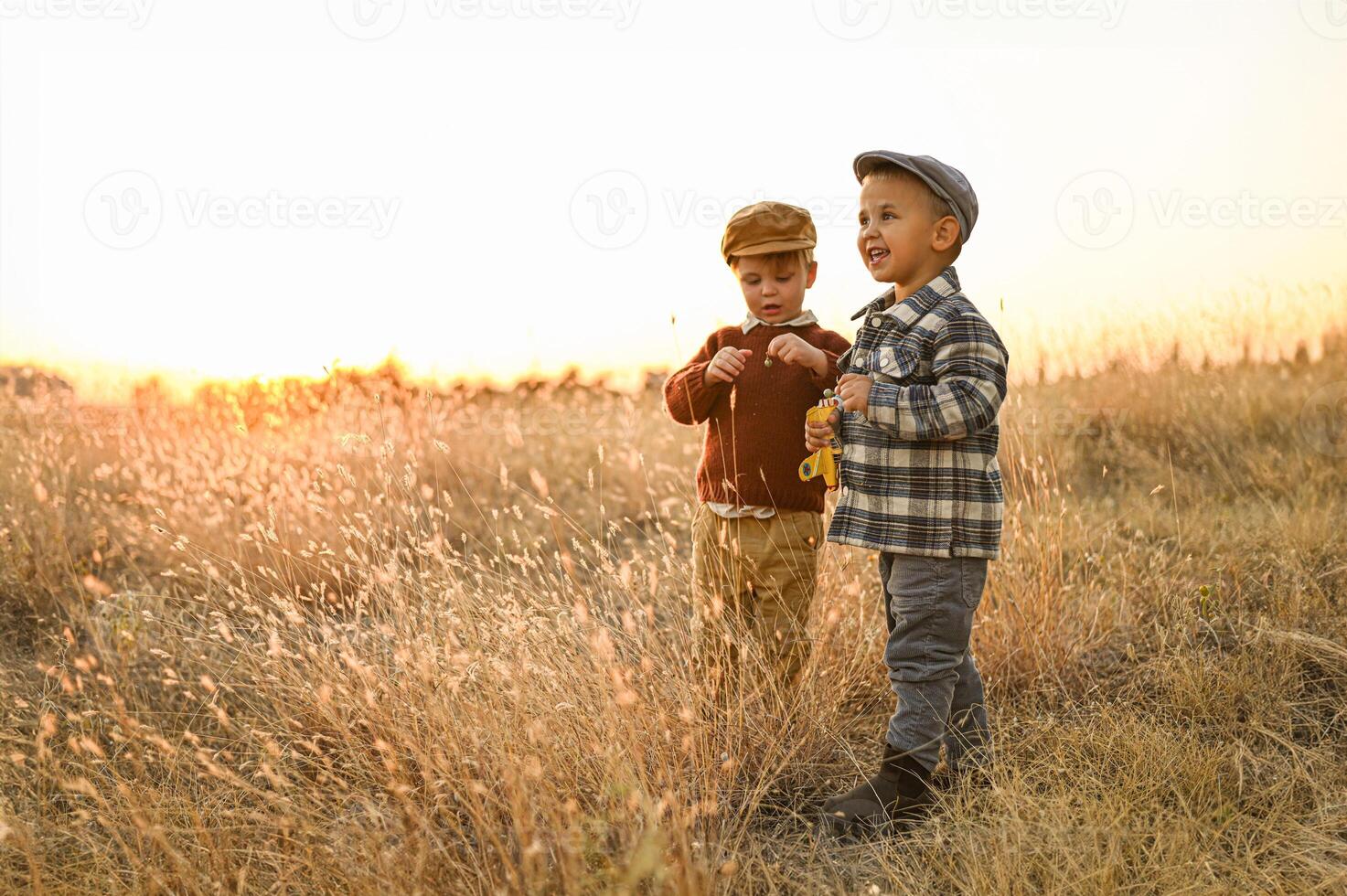Two little boys play joyfully in a golden field at sunset, laughing as they run with a large teddy bear. photo