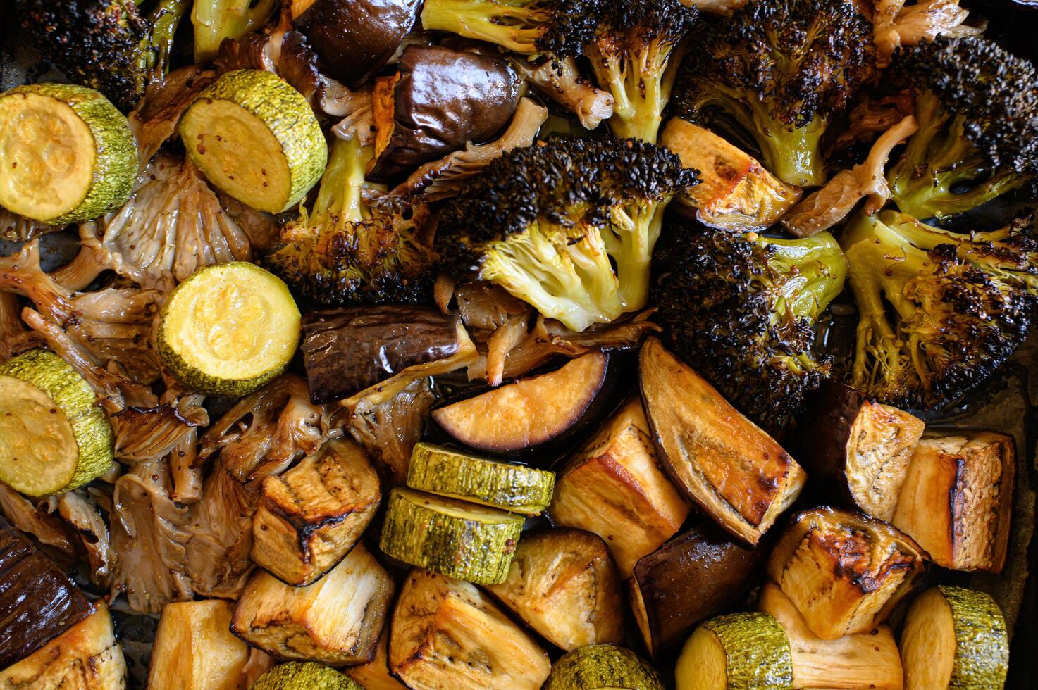 Golden-brown roasted eggplant, zucchini, mushrooms, and broccoli on a tray, showcasing their crispy texture and vibrant colors. photo