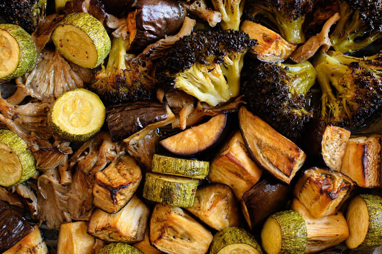 A colorful array of roasted vegetables, including broccoli, zucchini, eggplant, and oyster mushrooms, drizzled with olive oil and herbs. photo
