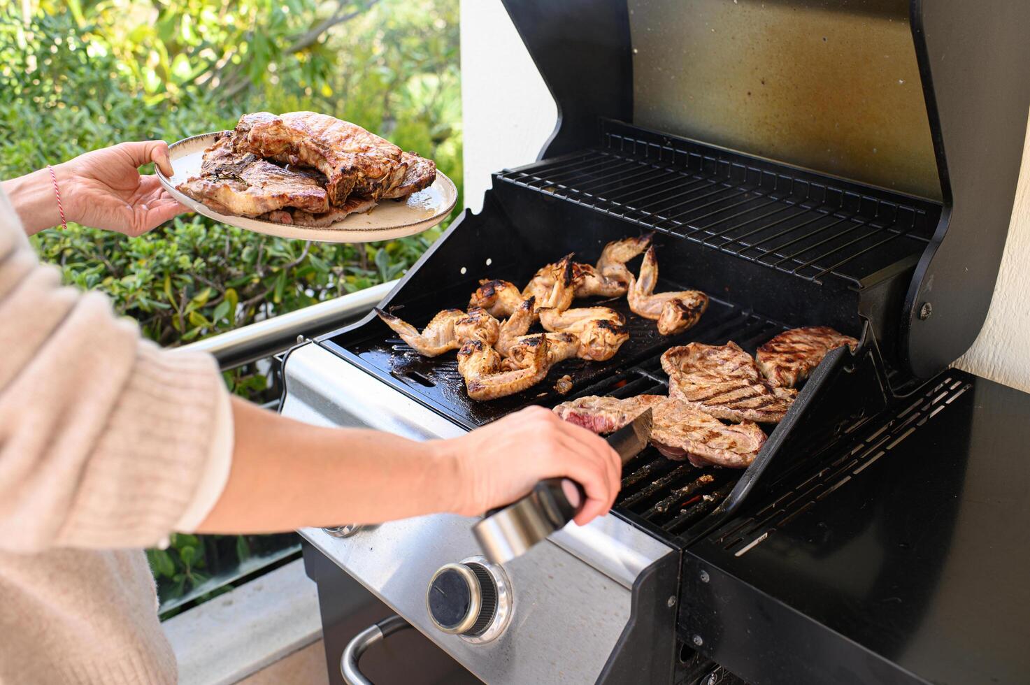 One hand grips metal tongs turning sizzling meat on the barbecue, the other balances a plate loaded with freshly grilled chicken and steak. photo