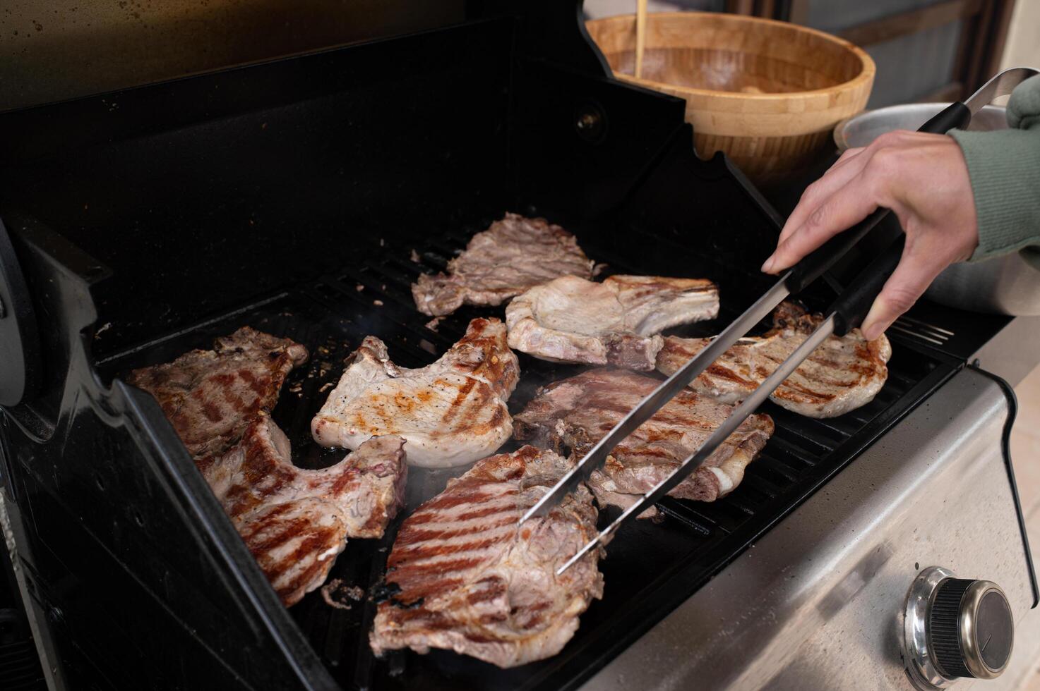 Tongs lifting a thick steak off the hot grill grates, grease dripping onto the coals, creating a smoky flare-up under golden hour sunlight. photo