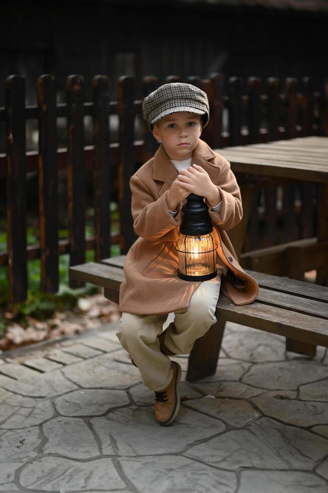 Dressed in old-fashioned clothes, the boy sitting on a bench with a lantern. photo