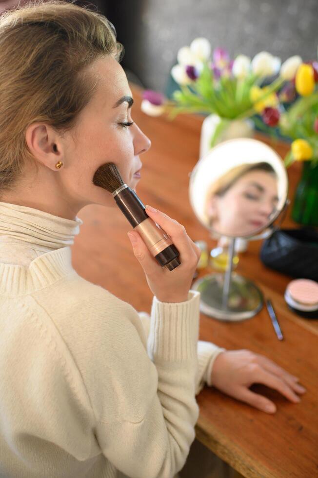 Woman applying bronzer with a brush while sitting at a table full of beauty products. photo