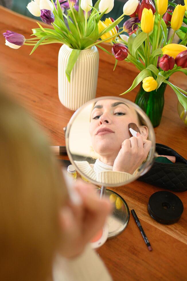 A young woman with a makeup compact in hand, looking at her reflection before applying blush. photo