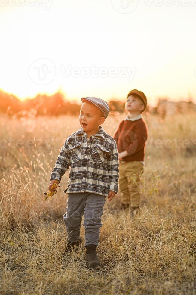 Two boys wearing kippahs stand side by side in a golden field at sunset, silhouetted against the warm evening light. photo