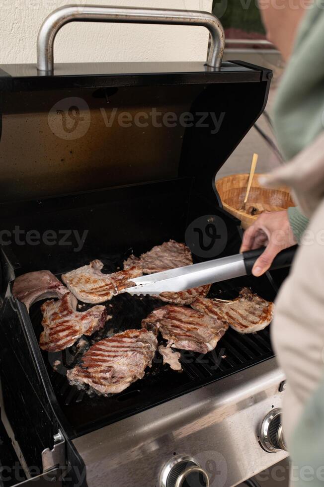 Woman leaning into the smoke, carefully turning grilled chicken with tongs, concentration on his face and flames flickering below. photo