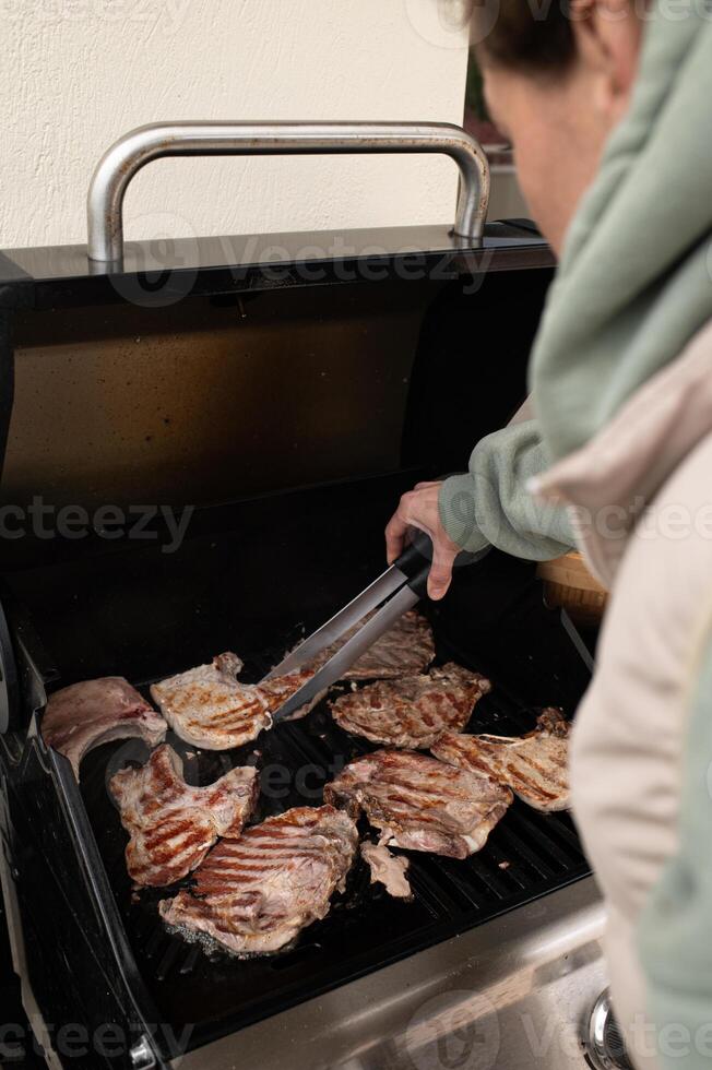 With tongs in hand, a man crouches slightly over the barbecue, flipping meat as smoke and sunlight mix in the summer air. photo