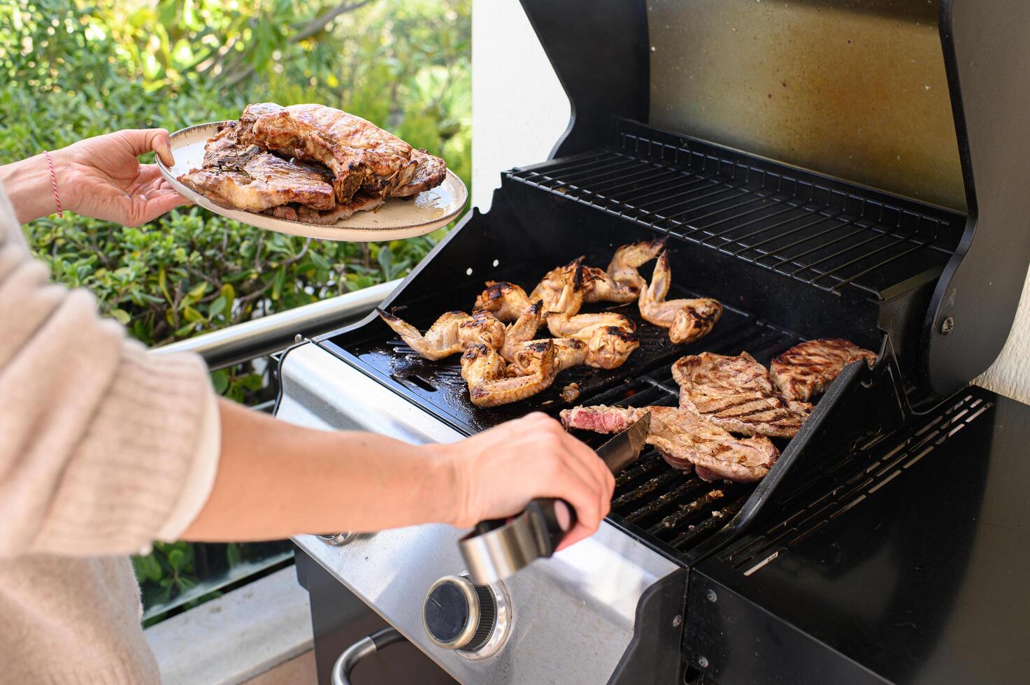Over the smoky grill, hands work quickly tongs flip meat as a full plate of grilled pieces rests in the other hand, ready to serve. photo