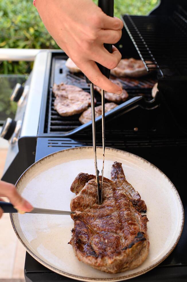 Hands slice into a freshly grilled piece of meat, holding it steady with metal tongs as juices run onto the cutting board. photo