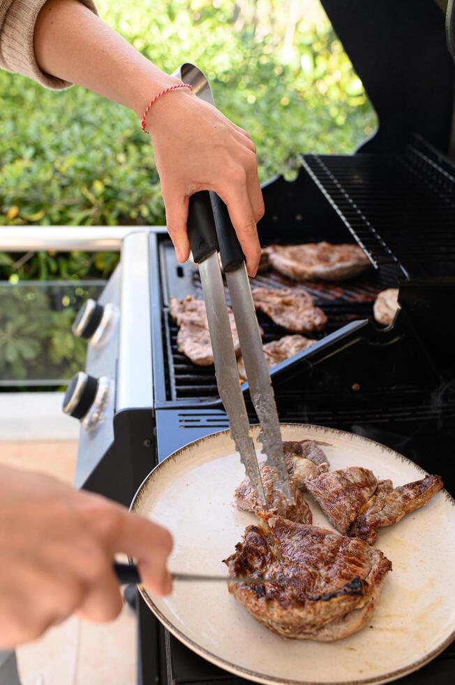 A perfectly seared steak is being cut with a sharp knife, one hand gripping tongs to hold the meat in place. photo
