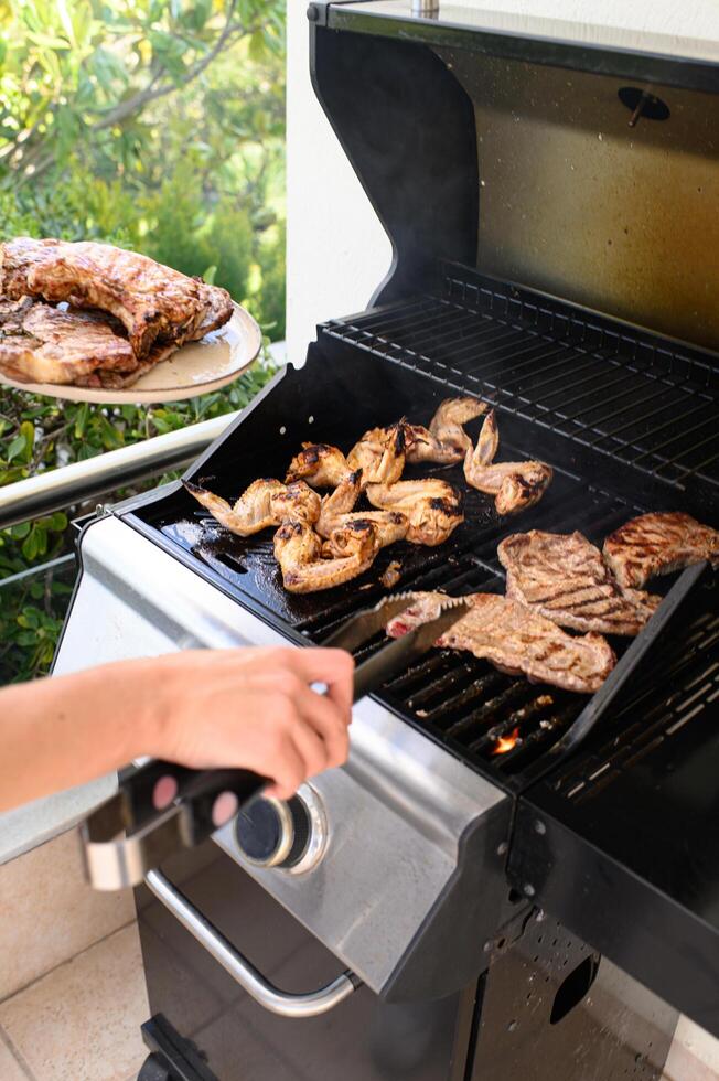 Hands hover over a hot grill, flipping juicy chicken and meat with tongs, while the other hand holds a plate full of perfectly grilled meat photo