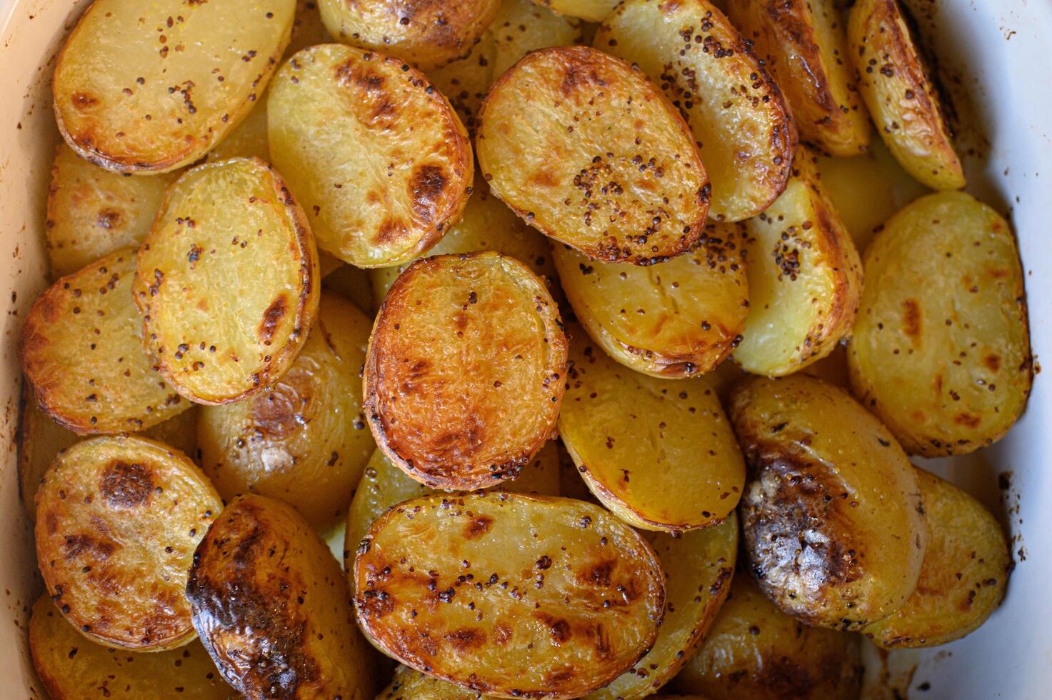 Close-up of rustic roasted potatoes coated in mustard and herbs, with crispy golden edges and a warm, hearty look photo