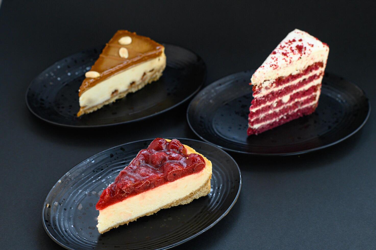 Elegant slices of cherry and caramel cheesecake with a red velvet cake, styled on a dark background with rich lighting. photo