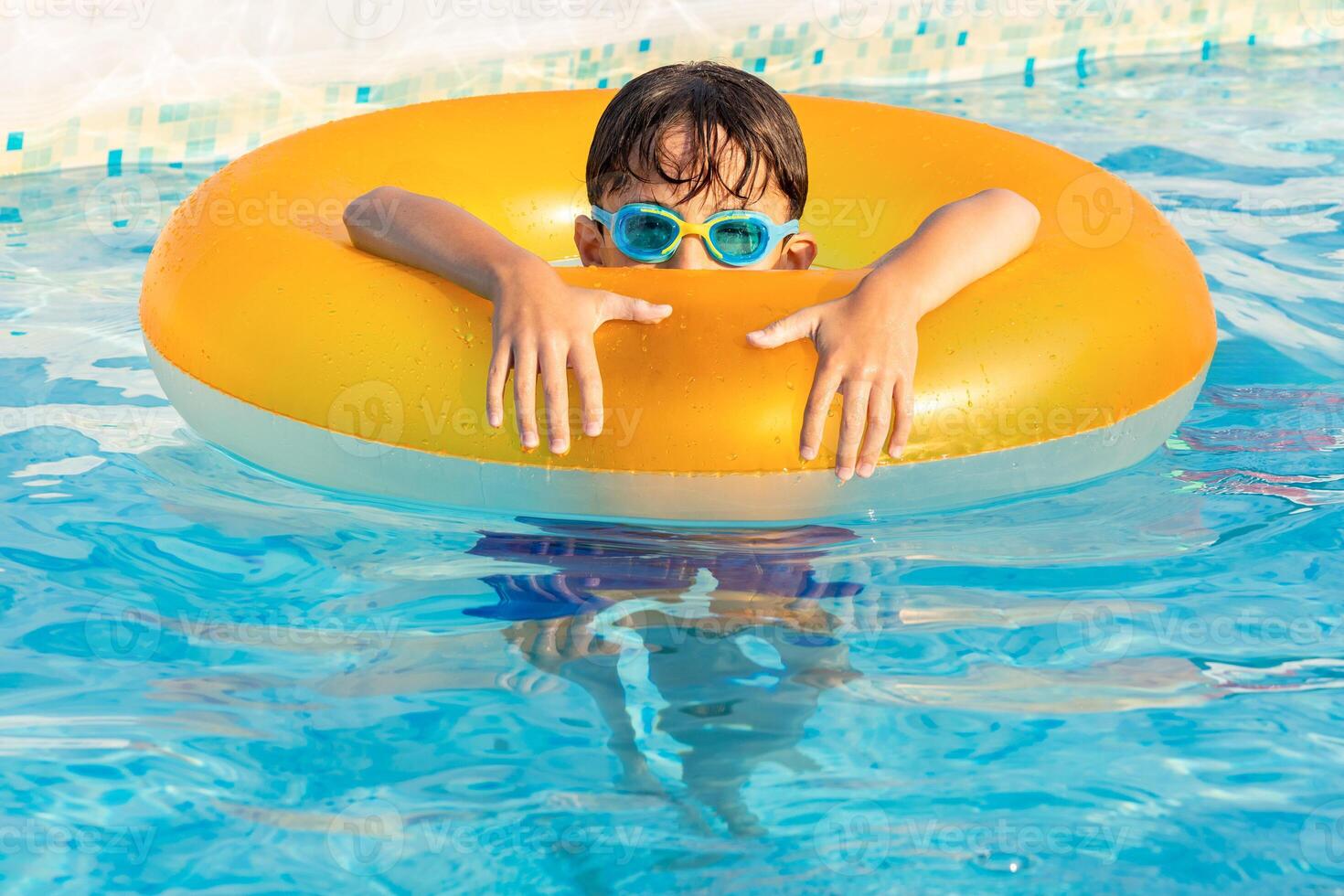 Child wearing swimming goggles relaxing in a pool with an inflatable ring on a sunny day photo