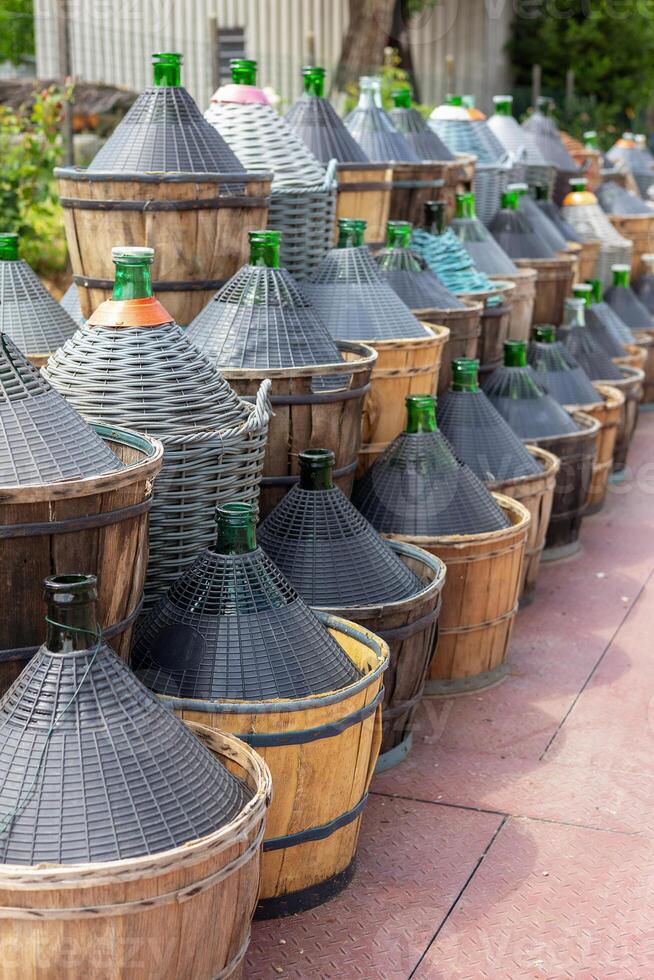 Traditional demijohn bottles in wicker baskets used for wine or olive oil storage, arranged outdoors in rustic setting. photo