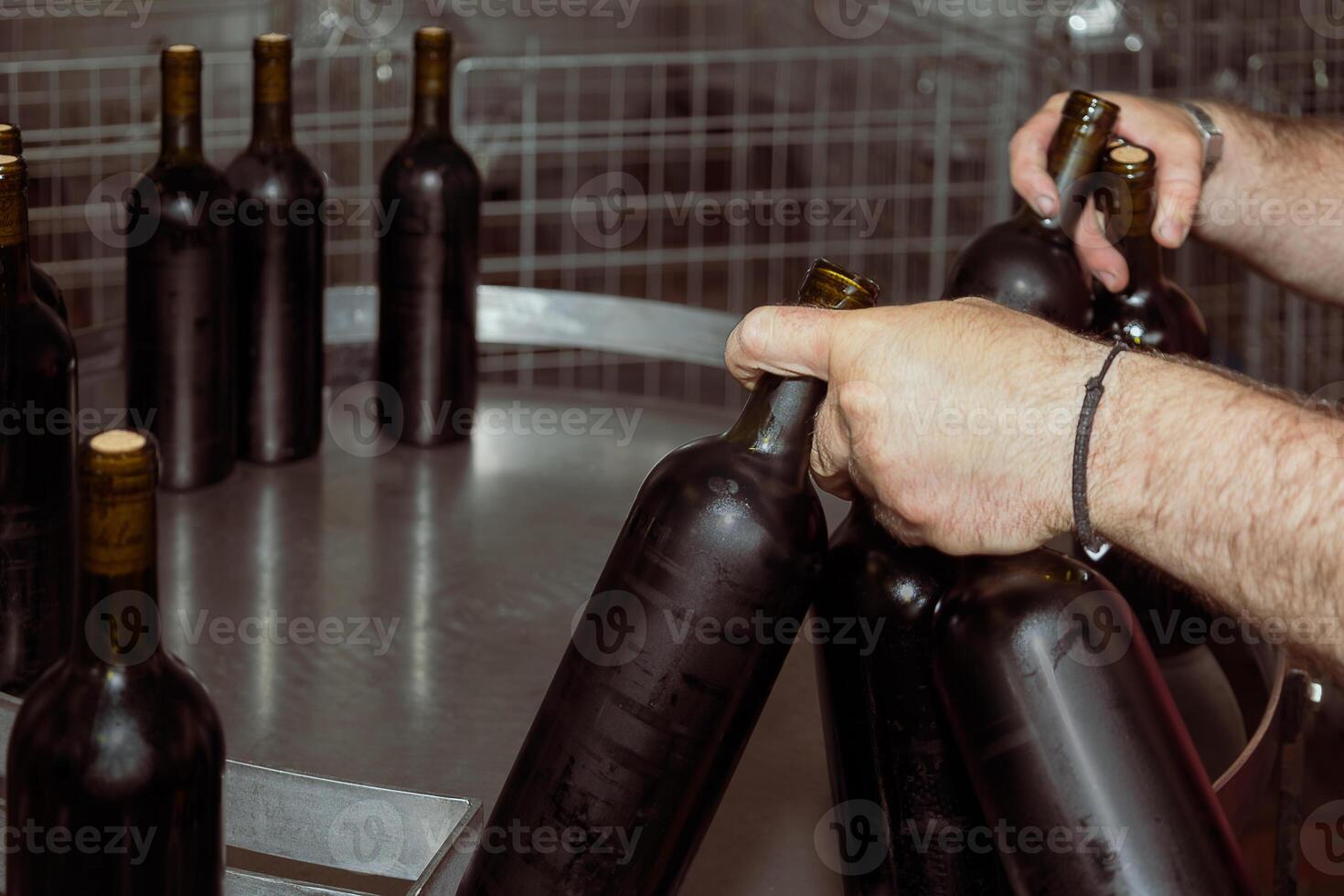 Winemaker placing bottles of red wine on metal table in winery photo