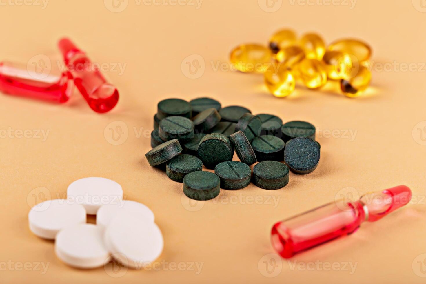Green spirulina tablets, white pills, yellow softgel and red ampoules on beige background. Vibrant display for health, wellness, or pharmaceutical advertising. Colorful health supplements and ampoules photo
