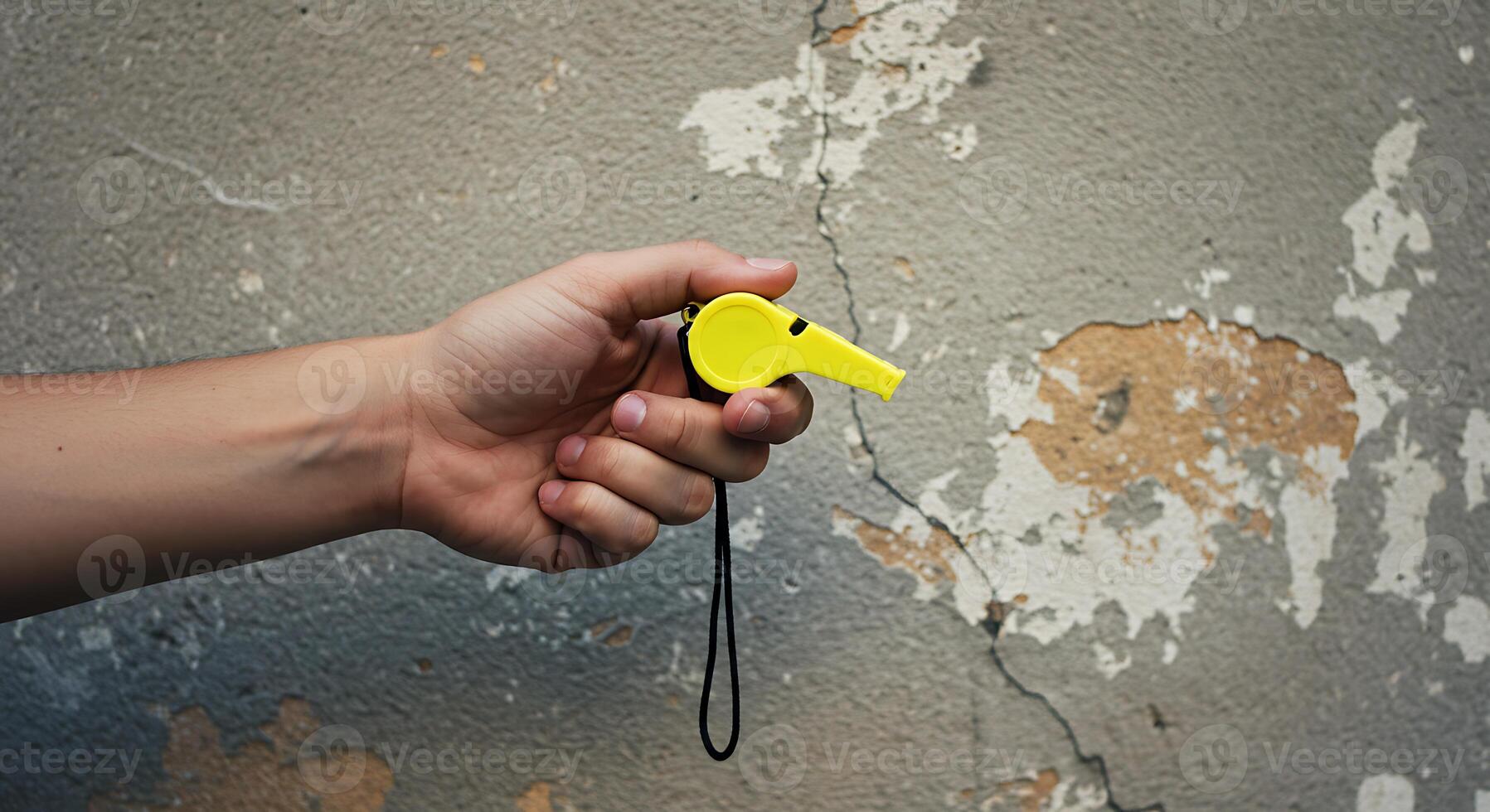 Hand Holding a Yellow Whistle Against a Weathered Wall photo