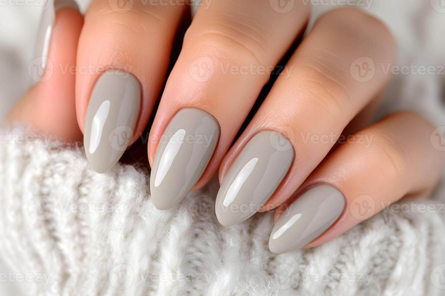 Elegant manicure showcasing smooth, almond-shaped nails painted in a soft gray color against a cozy knitted backdrop photo