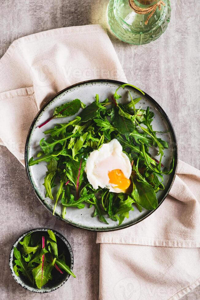 Leafy greens and poached egg on a plate on a table top and vertical view photo