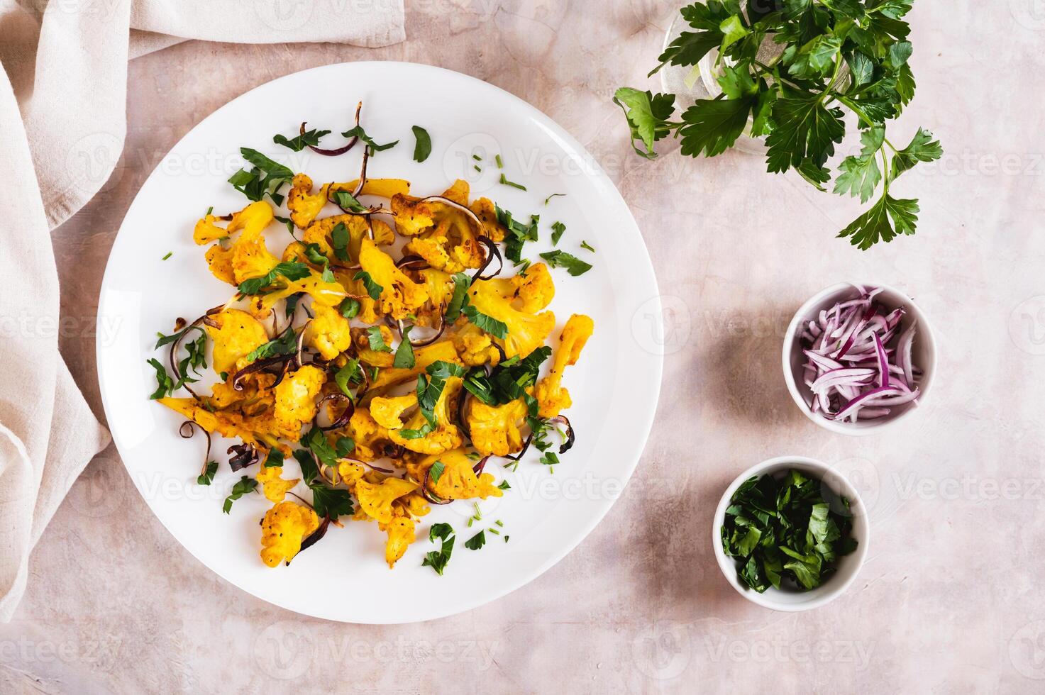 Baked small cauliflower steaks with onions and herbs on a plate on the table top view photo
