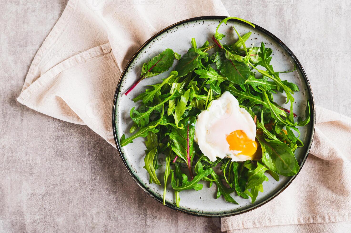 Close up of poached egg in arugula and chard leaves on a plate on a table top view photo