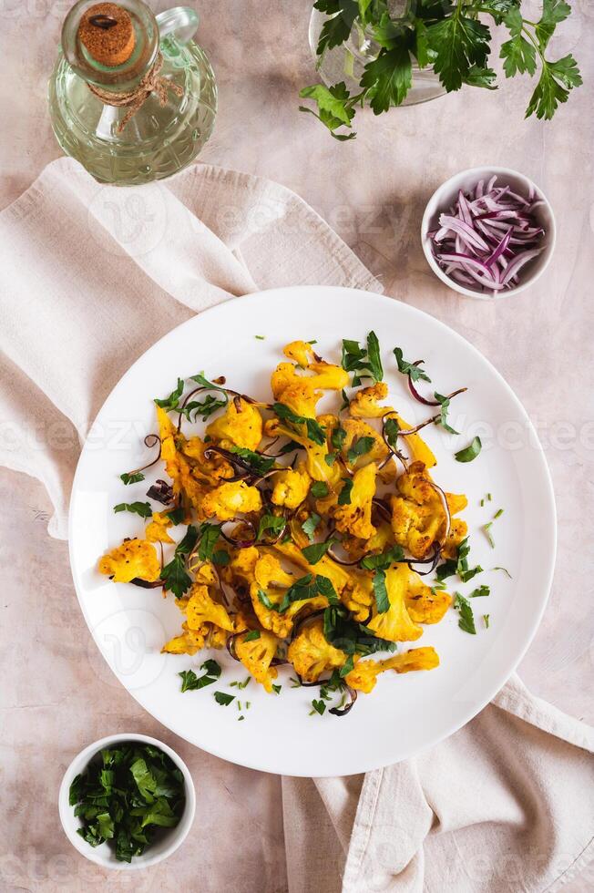 Baked spicy cauliflower with onions and parsley on a plate on the table top and vertical view photo